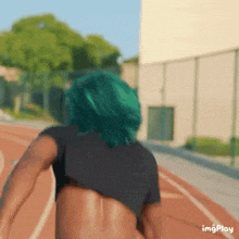 a woman with green hair is running on a track without a shirt on