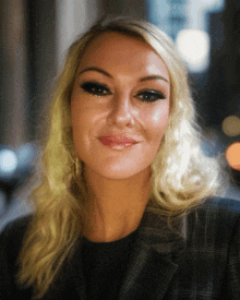 a blonde woman wearing a plaid jacket is smiling