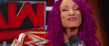 a woman with purple hair is talking into a microphone while holding a wrestling championship .