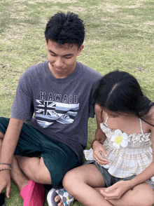 a boy wearing a hawaii shirt sits next to a little girl