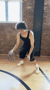 a man dribbles a basketball on a court with a brick wall in the background