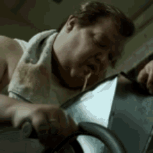 a man with a towel around his neck is riding an exercise bike and eating noodles .