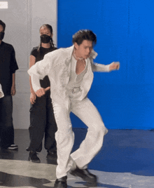 a man in a white suit dancing in front of a blue wall