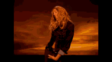 a woman in a black dress stands in front of a sunset sky