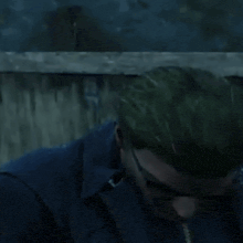 a man wearing sunglasses and a blue jacket is sitting in front of a wooden fence .