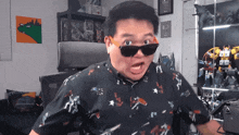 a man wearing sunglasses and a shirt with a robot print is making a funny face