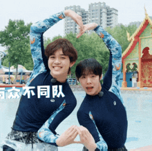 two young men are making a heart shape with their arms in front of a pool