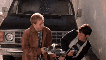 two men are standing in front of a van and one of them is wearing a black shirt that says n.o.r.