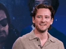 a man in a sweater is smiling in front of a blurred image of another man .