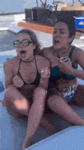 two women in bikinis are sitting on a boat with one holding a can of beer