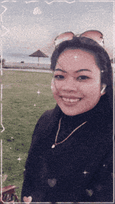 a woman wearing sunglasses and a necklace smiles in front of a beach
