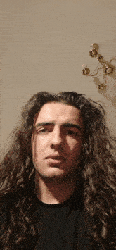 a man with long curly hair is standing in front of a wall