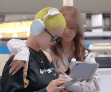 a woman wearing headphones looks at a tablet next to a man wearing a nike shirt