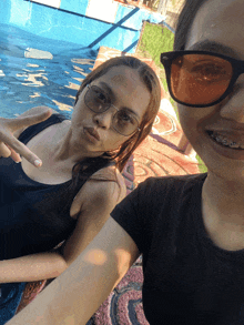 two girls wearing sunglasses pose for a photo in front of a pool