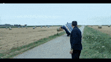 a man stands on the side of a road looking at a car that is on its side in a field