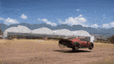 a red car is driving on a dirt road