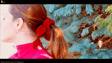 a woman wearing a red sweater and a red ribbon in her hair is standing in front of a blue pine tree