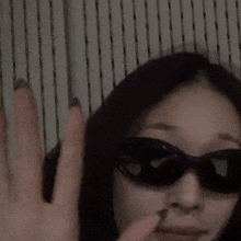 a close up of a woman wearing sunglasses and making a stop sign .