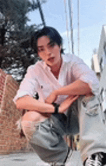 a young man in a white shirt is kneeling down on the sidewalk .