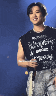 a man wearing a black balenciaga tank top smiles on stage