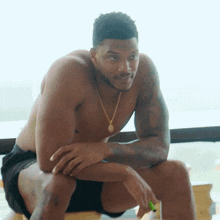 a shirtless man with a necklace around his neck sits on a table