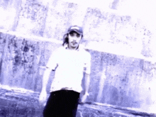 a man wearing a white shirt and a black hat stands in front of a wall