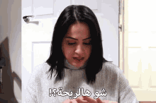 a woman wearing a grey sweater has arabic writing on her chest