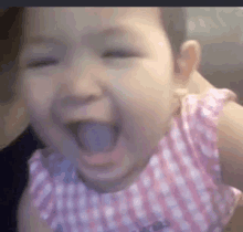 a baby girl is laughing with her mouth open and wearing a pink dress .