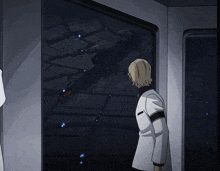 a man in a white coat stands in front of a window looking out