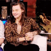 a man with long hair is wearing a leopard print shirt and sitting on a couch .