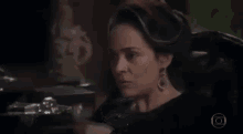 a woman in a black dress and earrings is sitting in a dark room .