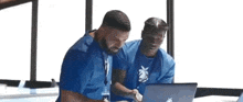 two men are standing next to each other looking at a laptop .