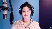 a woman wearing headphones and a pink jacket stands in front of a microphone