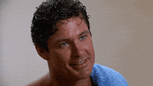 a man with curly hair and blue eyes is smiling with a blue towel around his neck