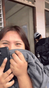 a woman is covering her mouth with a blanket while holding a cell phone .