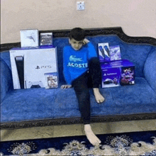 a young boy in a blue lacoste sweater sits on a blue couch surrounded by ps5 boxes