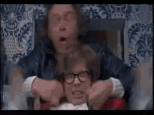 a man with glasses is holding another man 's neck in a room .