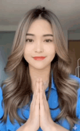 a woman with long hair is wearing a blue shirt and praying with her hands together .
