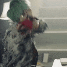 a person with green hair is standing in a room holding a red object and a microphone .