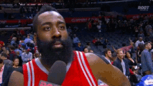 a man with a beard is talking into a microphone at a basketball game sponsored by root sports