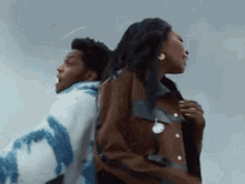 a man and a woman are standing back to back . the man is wearing a tie dye sweater .