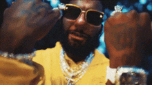 a man with a beard and sunglasses is wearing a yellow jacket and necklace .