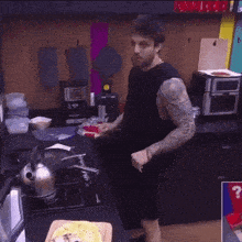 a man in a black tank top is standing in a kitchen with a kettle on the stove