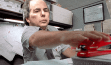 a man using a red stapler in an office space