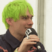 a man with green hair is holding a microphone with a r on it