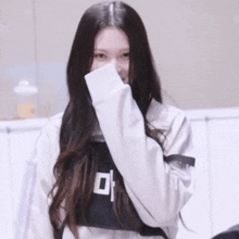 a woman wearing a white jacket and a black shirt with the letter m on it covering her face