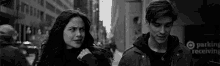 a black and white photo of a man and a woman walking down the street .