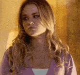 a woman with long blonde hair is wearing a purple sweater and a white tank top .