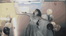a woman in a white dress is dancing in front of balloons and the word kamua creation is on the wall