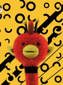 a red stuffed animal with a yellow beak is standing on a yellow background .